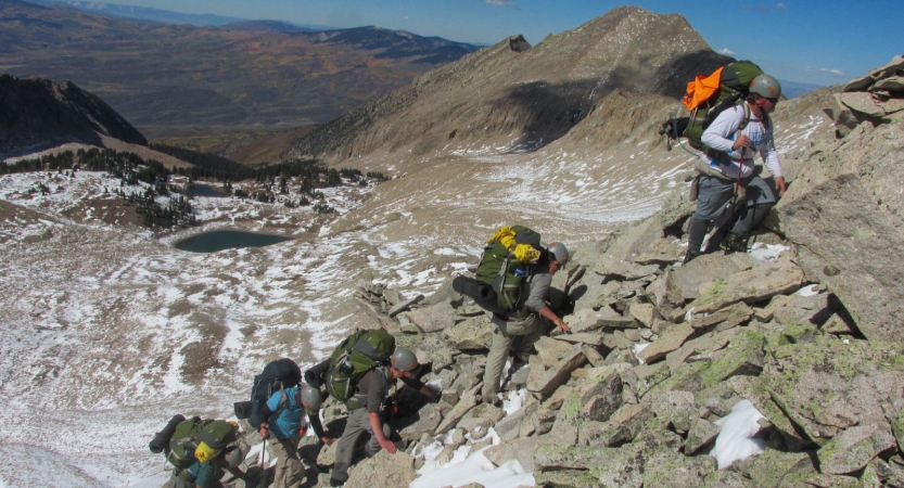 A group of people wearing safety gear make their way up a rocky landscape.